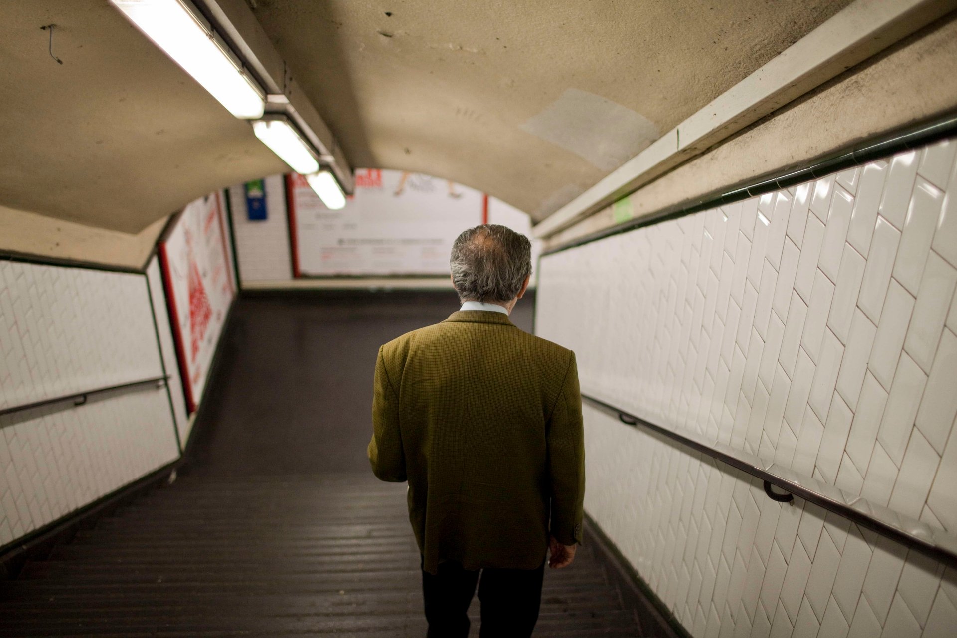 Older man descending Paris métro stairs, green jacket