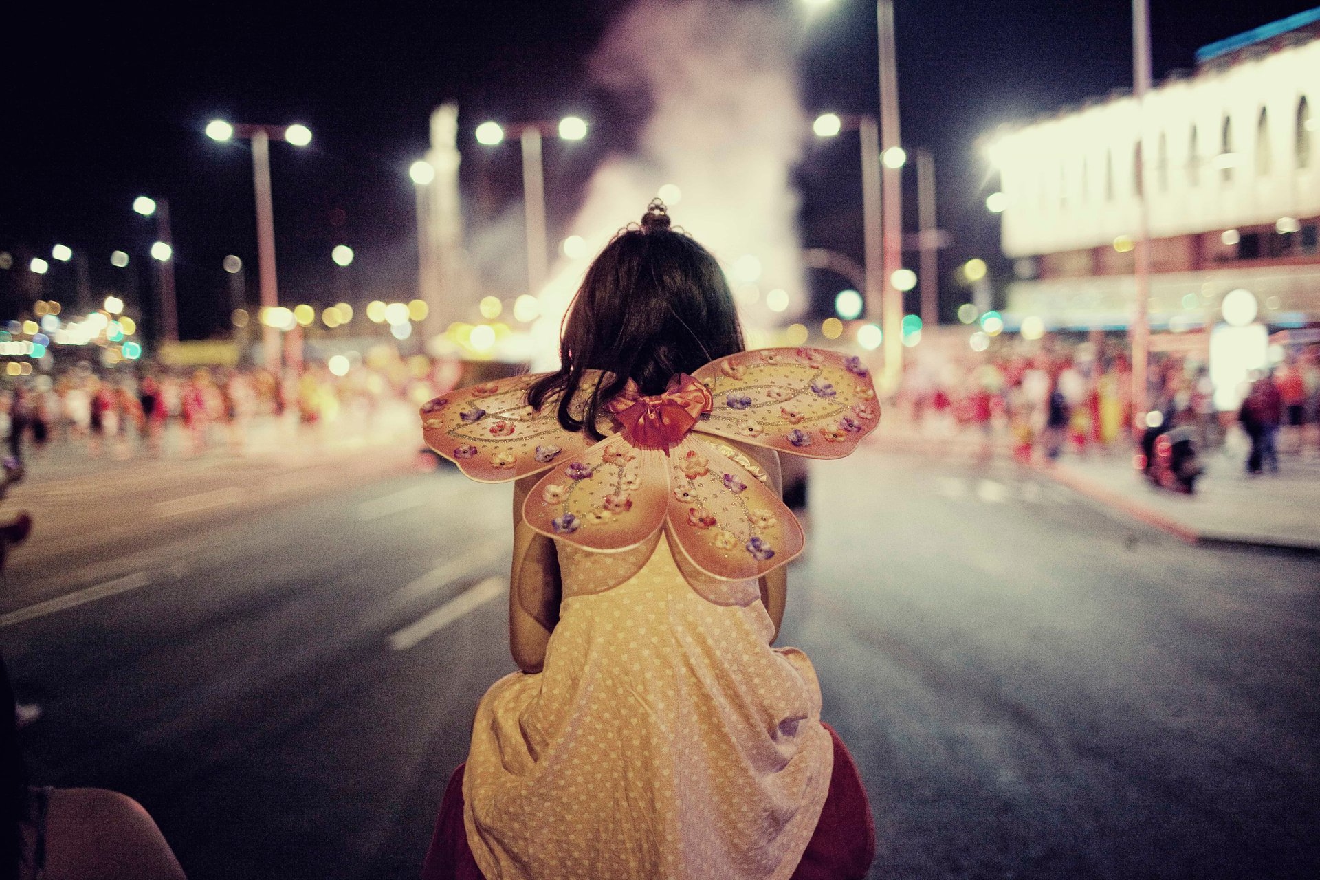 Child with butterfly wings on shoulders at night carnival