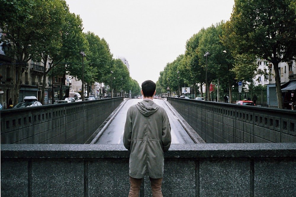 Man in hoodie at Parisian road overpass, symmetrical boulevard