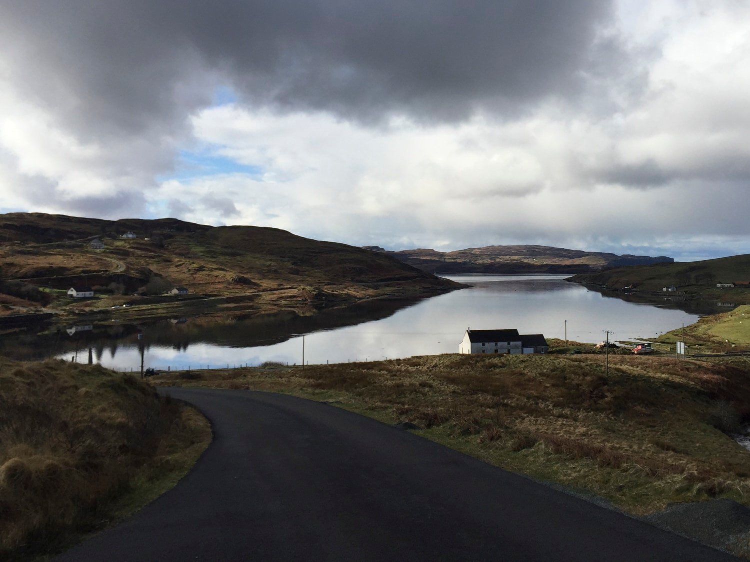 Narrow road curving toward loch and white farmhouse