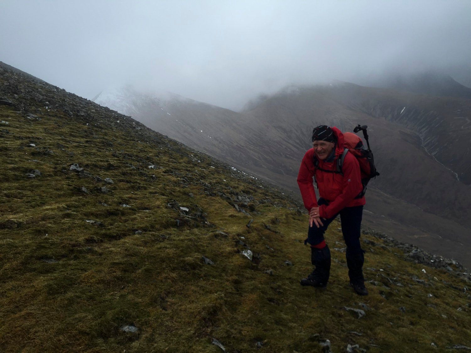 Hiker in red jacket climbing steep slope, grinning