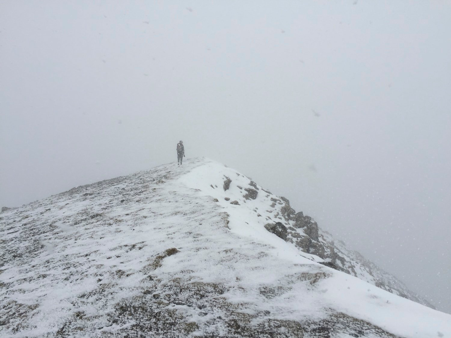 Solitary figure on snowy ridge, tiny against white expanse